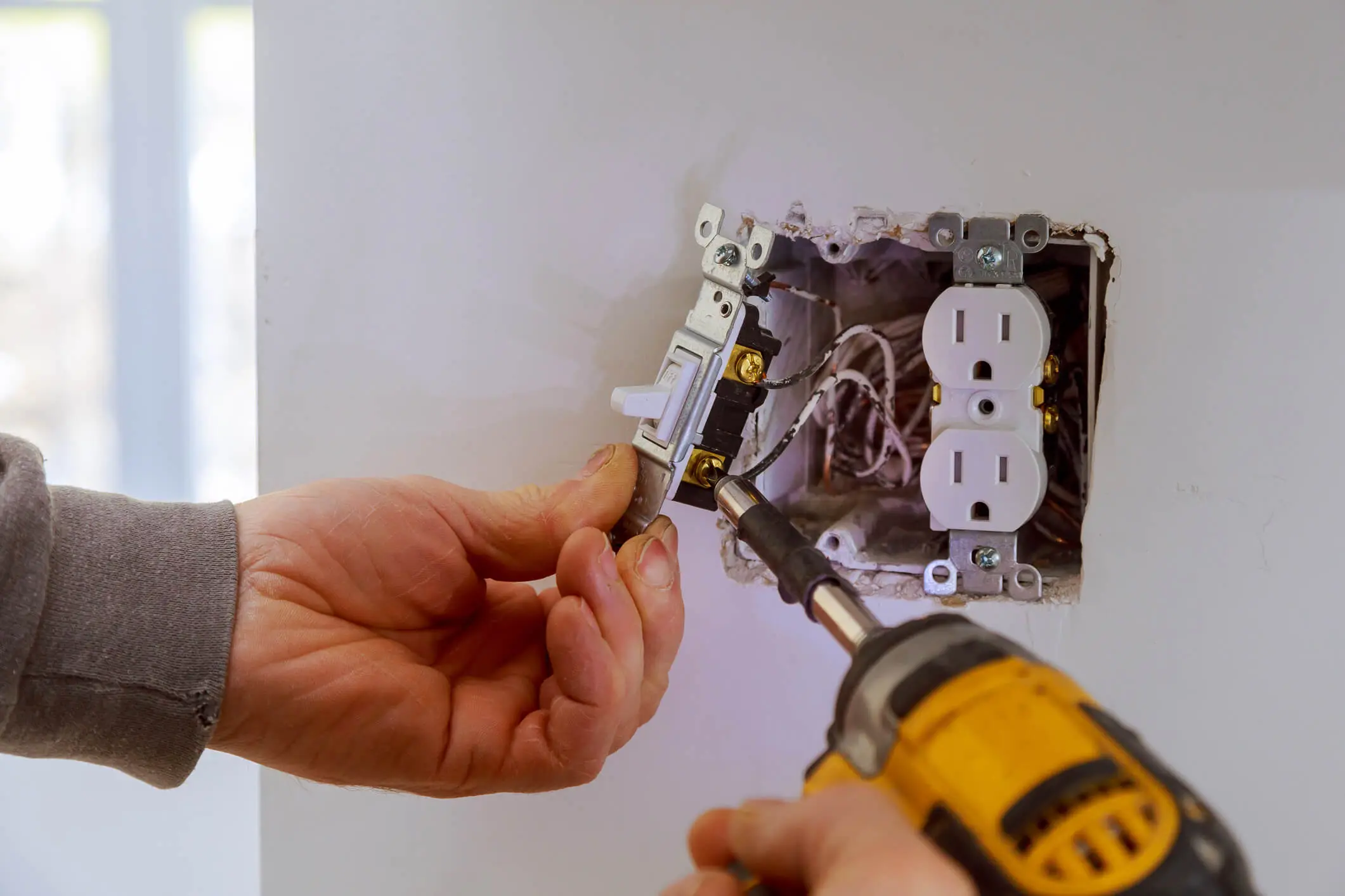 A person installs an electrical outlet using a power drill.