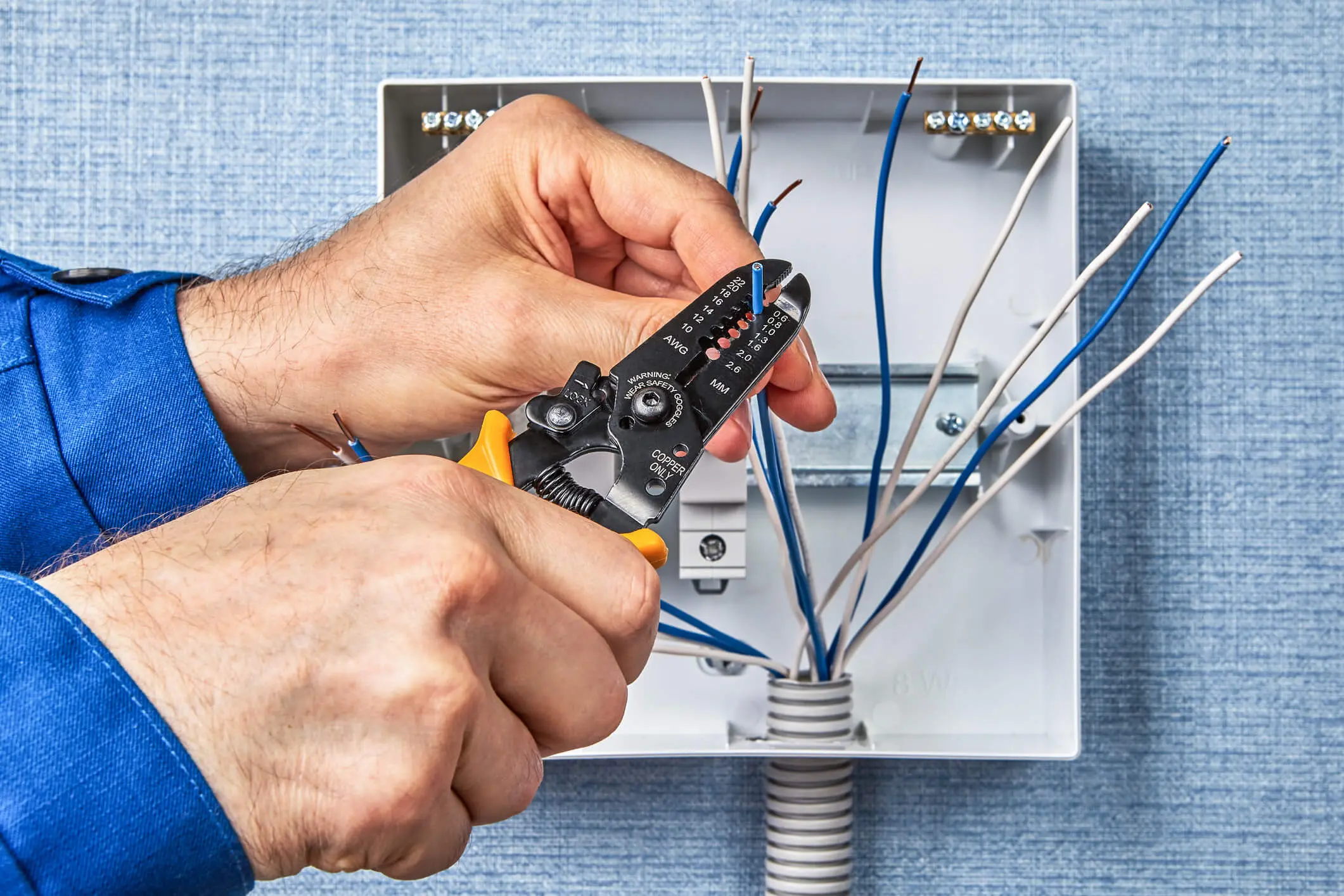 Person using wire strippers on electrical wires inside a junction box.