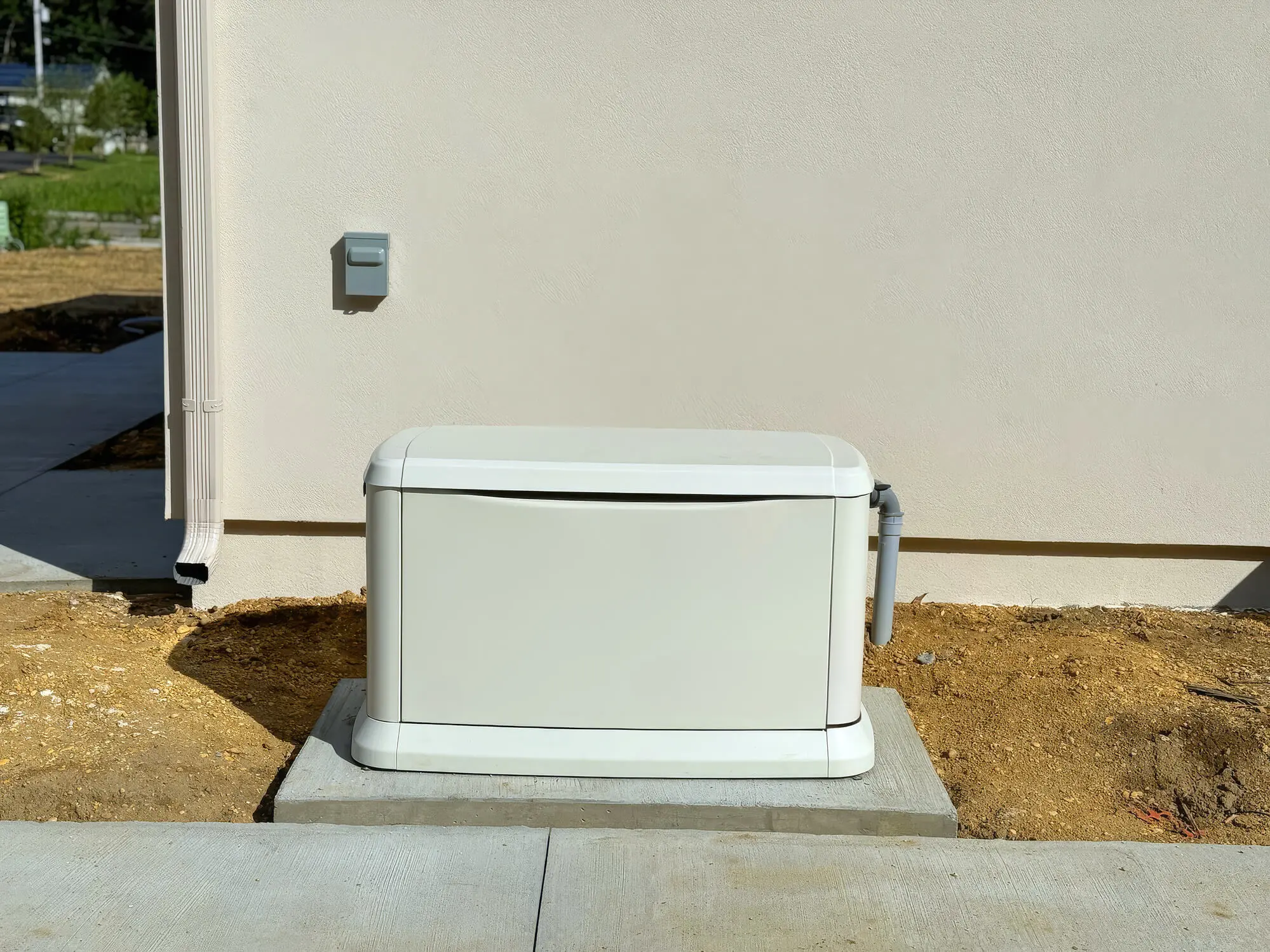A white electrical generator unit outside a building on a concrete base.