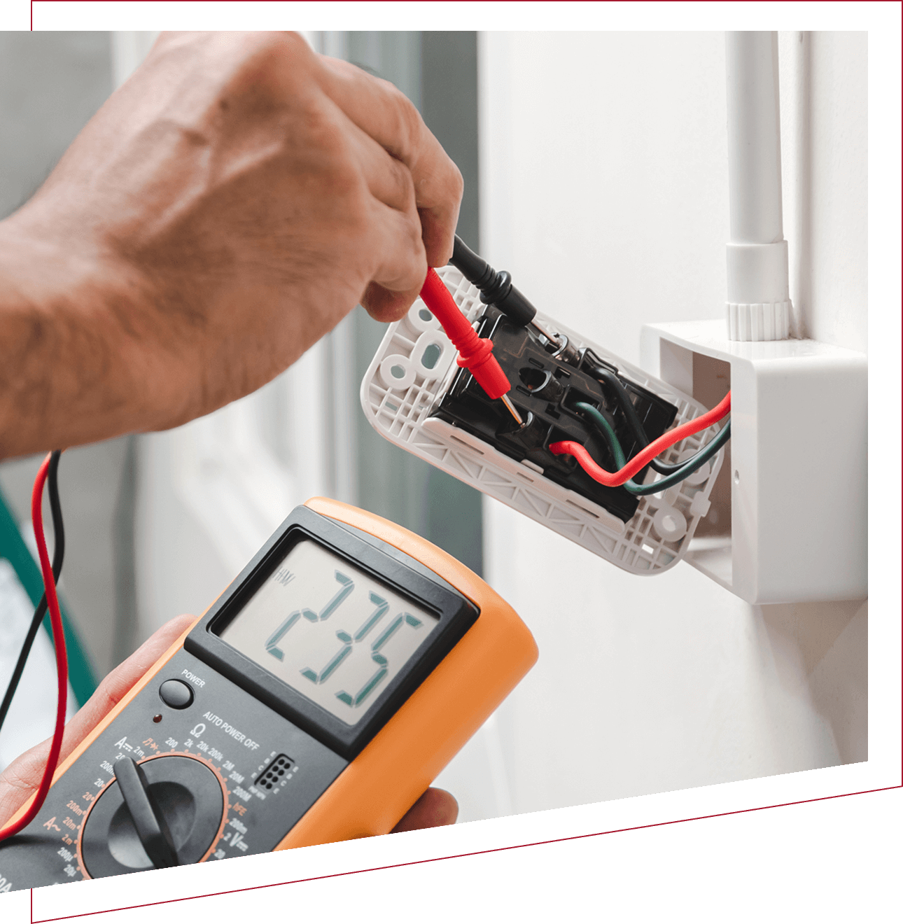 A hand using a multimeter to measure voltage in an electrical outlet.