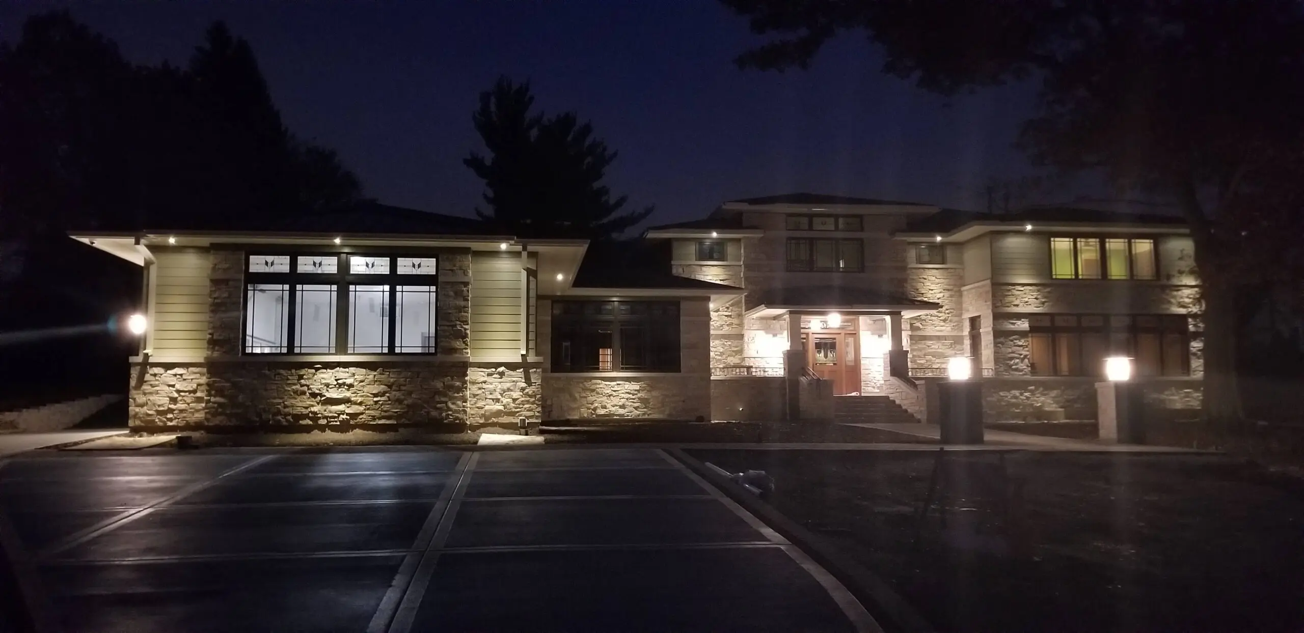 Modern house exterior illuminated at night with stone and wood accents.