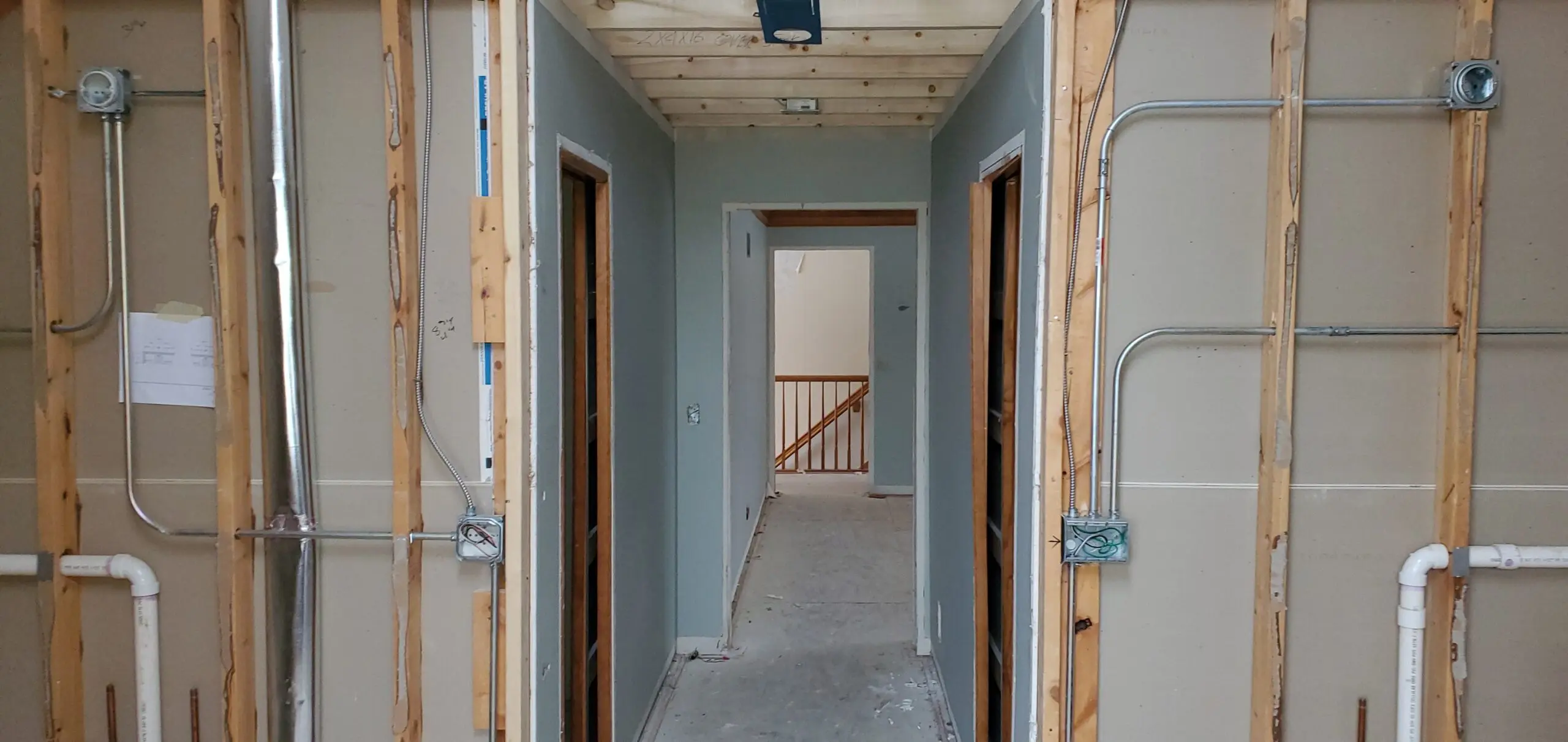 Interior hallway of a house under renovation with exposed wiring and unfinished walls.