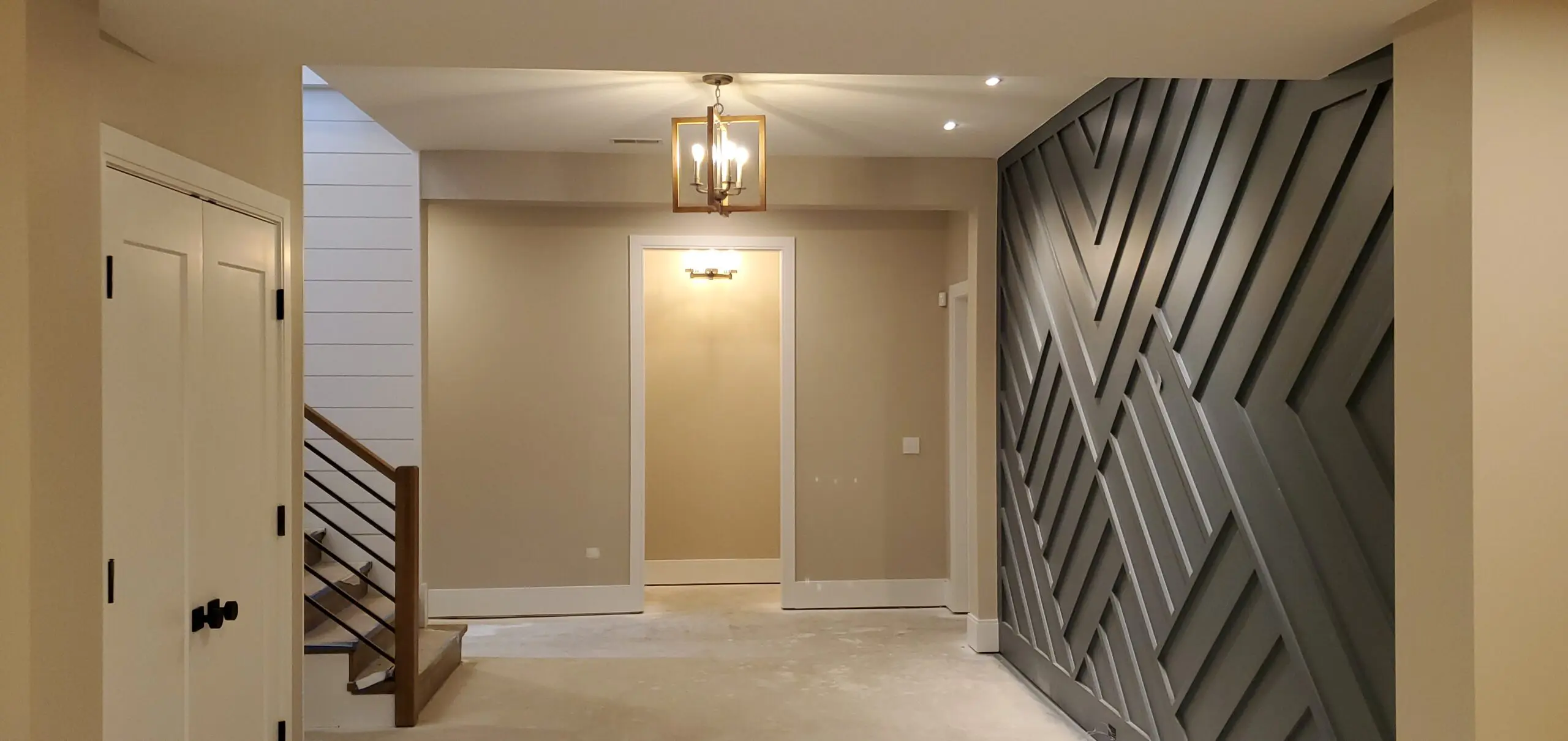 Modern beige hallway with geometric accent wall and chandelier lighting.