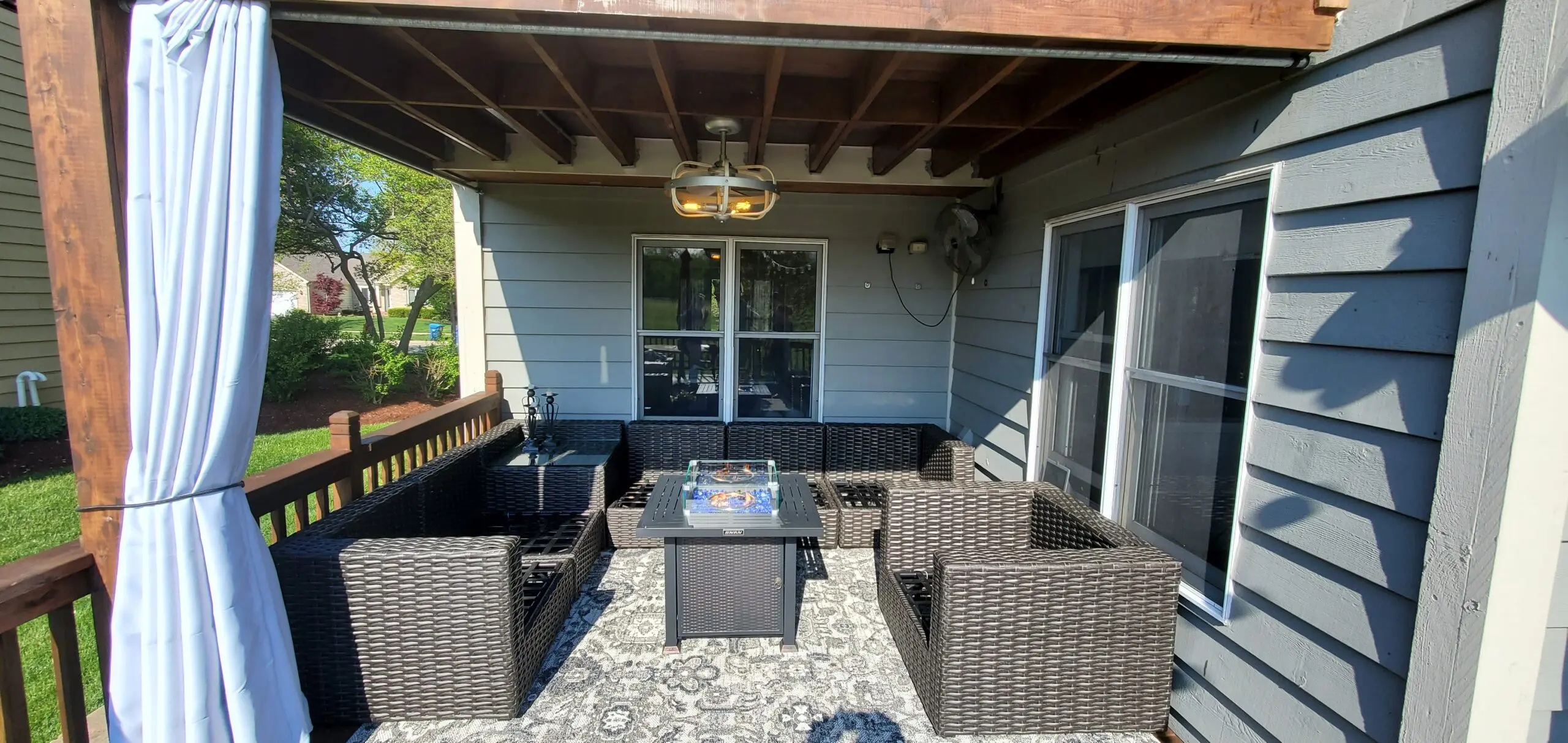 Cozy outdoor seating area with wicker furniture and a fire pit under a covered porch.