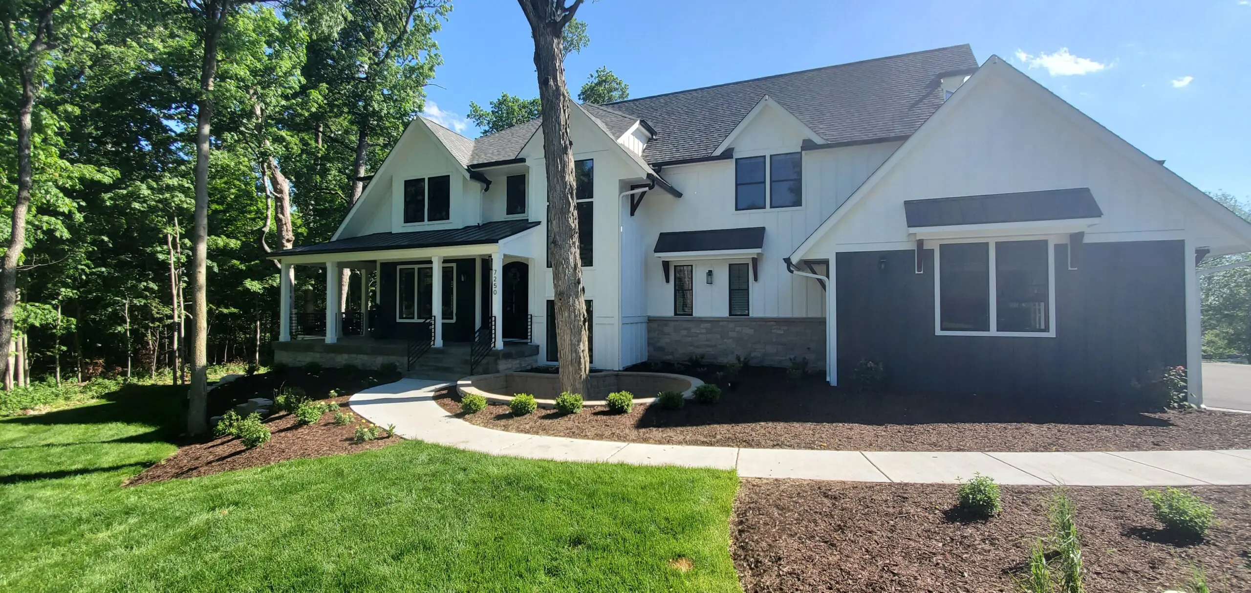 Modern white house with black roof and lush green lawn.