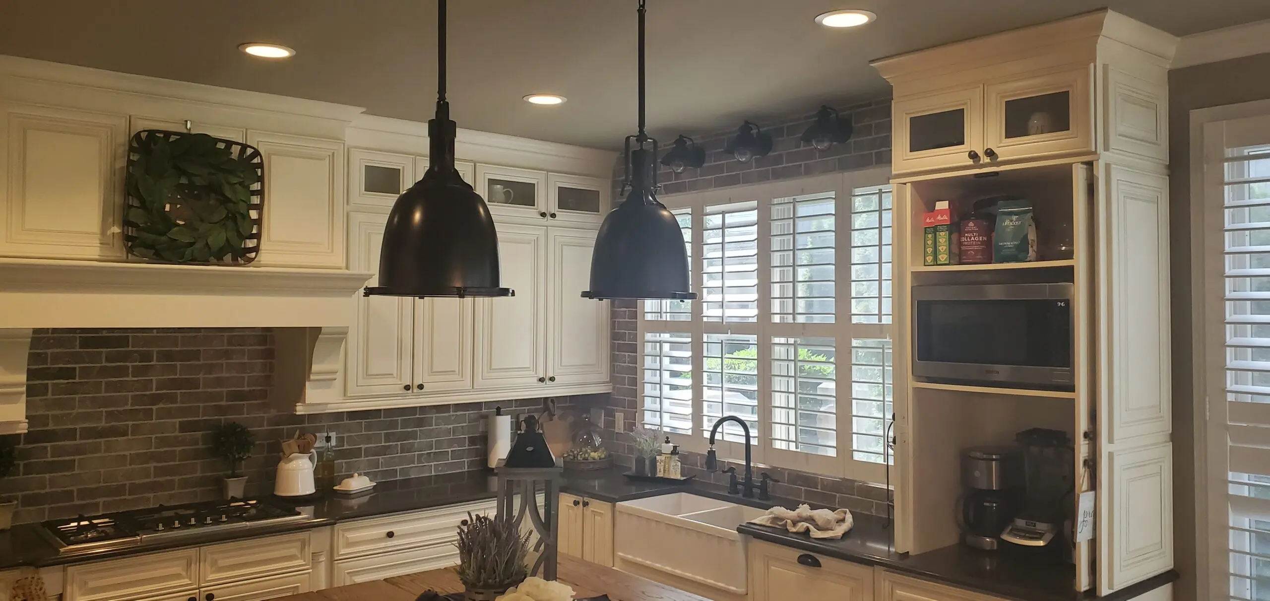 Cozy kitchen with white cabinets, farmhouse sink, and black pendant lights.