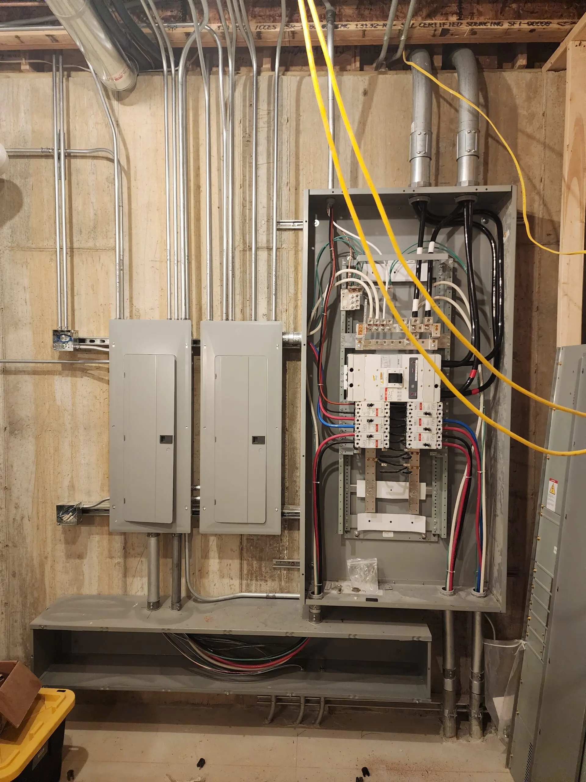 Open electrical panel with wiring and breakers beside closed panels.