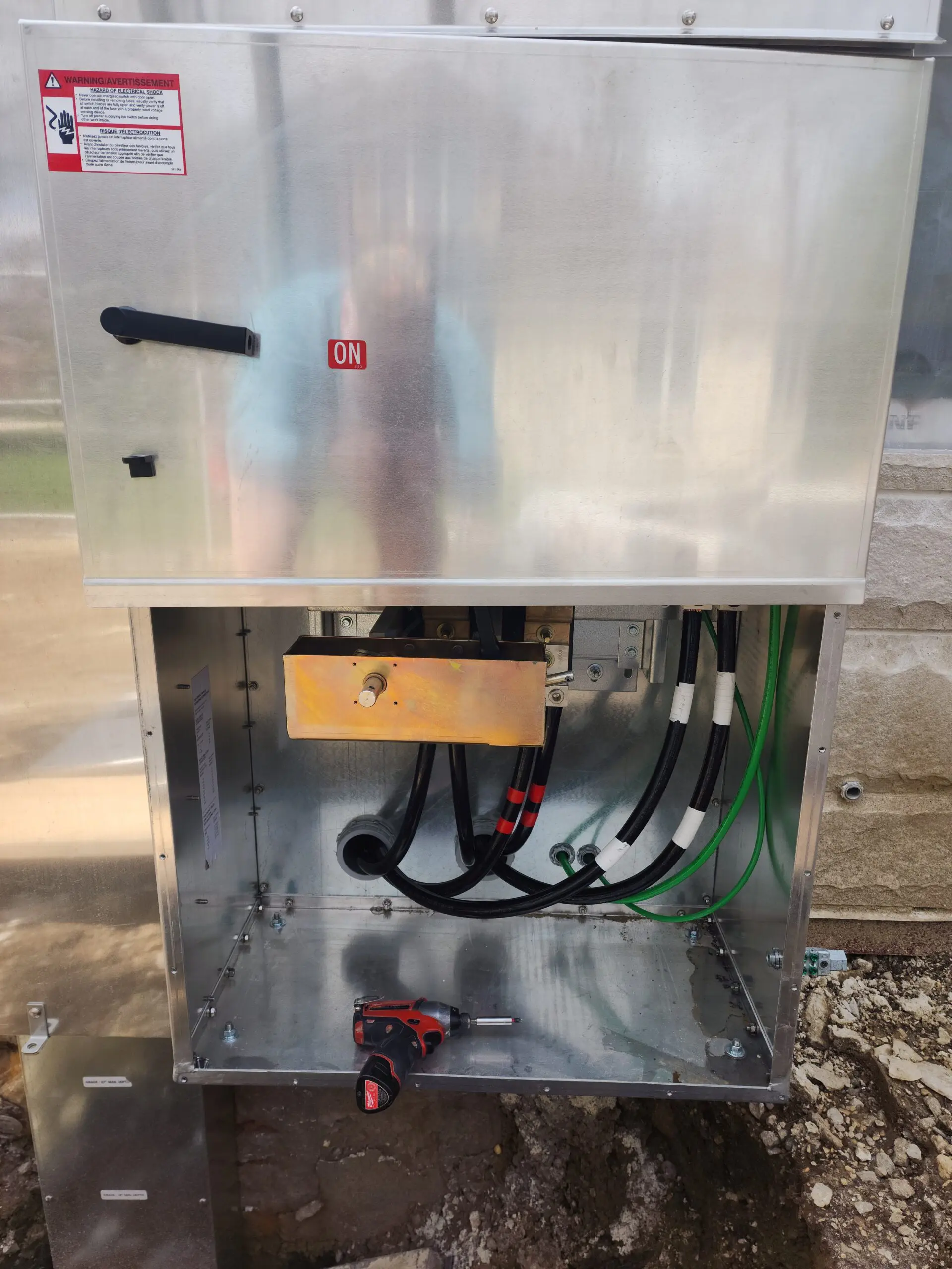 Electrical panel with wires and a wooden component inside a metal enclosure.